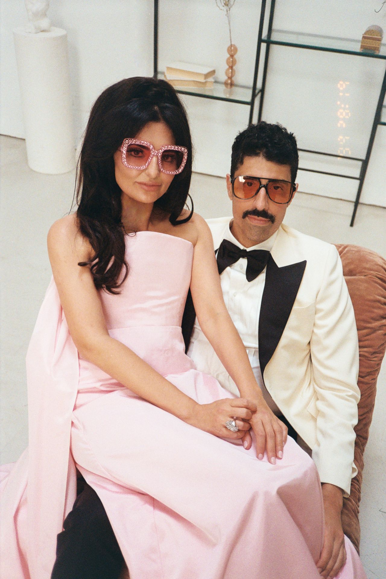 Roya and Mani sitting together, both wearing sunglasses in addition to their wedding outfits