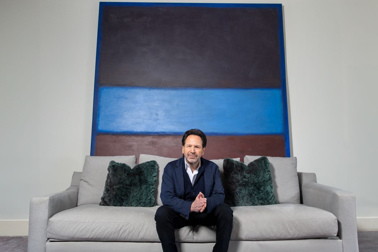 Barry Avrich poses sitting on a couch in front of a large Rothko painting.