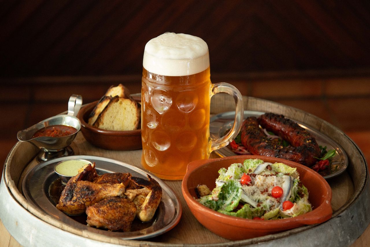 A tray loaded with a stein of beer, a bowl of salad and plates of chicken, sausages and bread