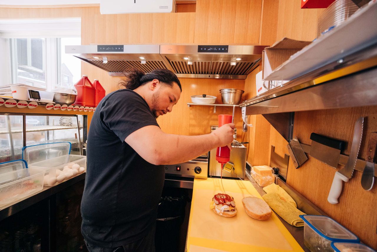 A person in a cafe kitchen squirts ketchup onto a breakfast sandwich