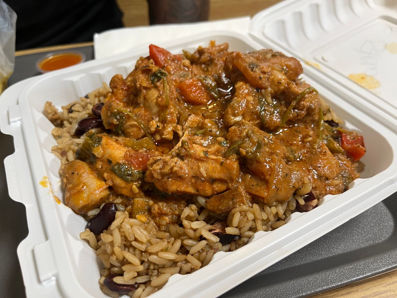 An order of stewed chicken with rice and peas in a takeout container