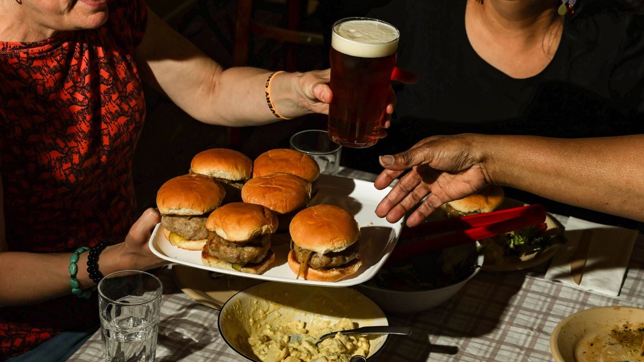 A person at a table holds a tray of burgers and a pint of beer