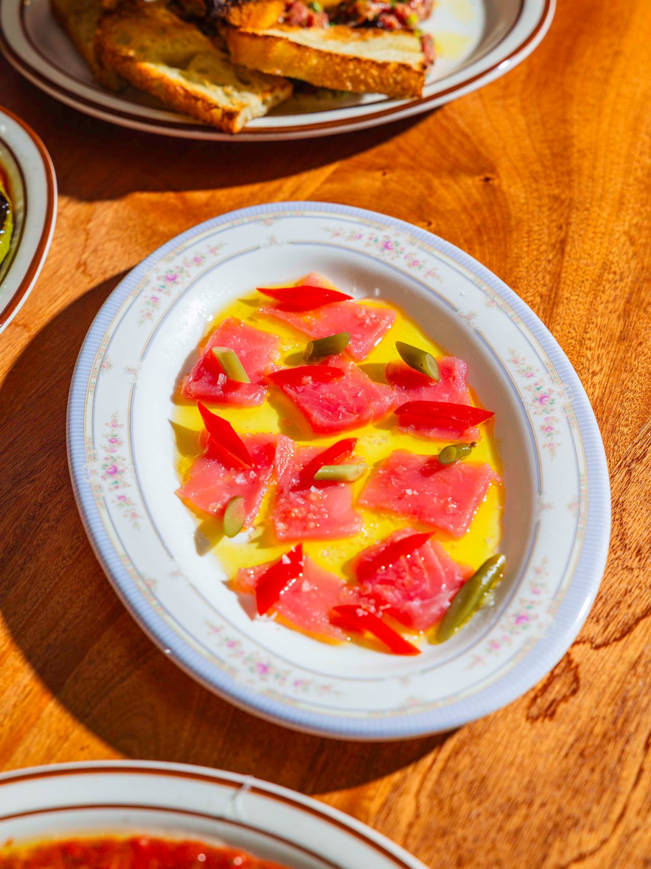 The blue fin crudo is a bright and balanced fancy bar snack. Centre-cut tuna is quick-cured in salt, sugar and lemon zest, then dressed with extra-virgin olive oil, and garnished with pickled Anaheim chiles and garlic scapes