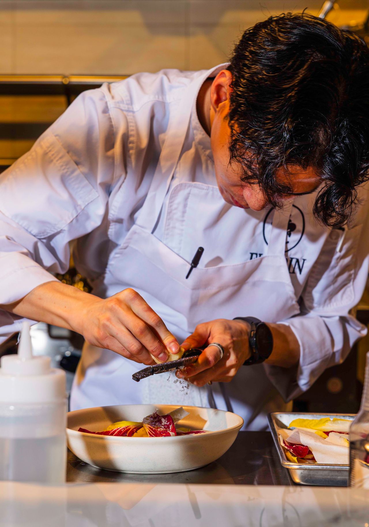 A chef grates cheese over a radicchio salad