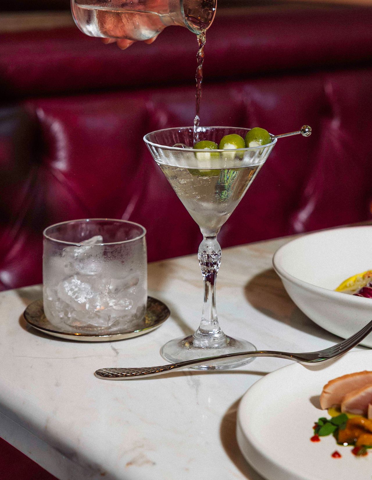 A person pours a martini from a carafe into a glass