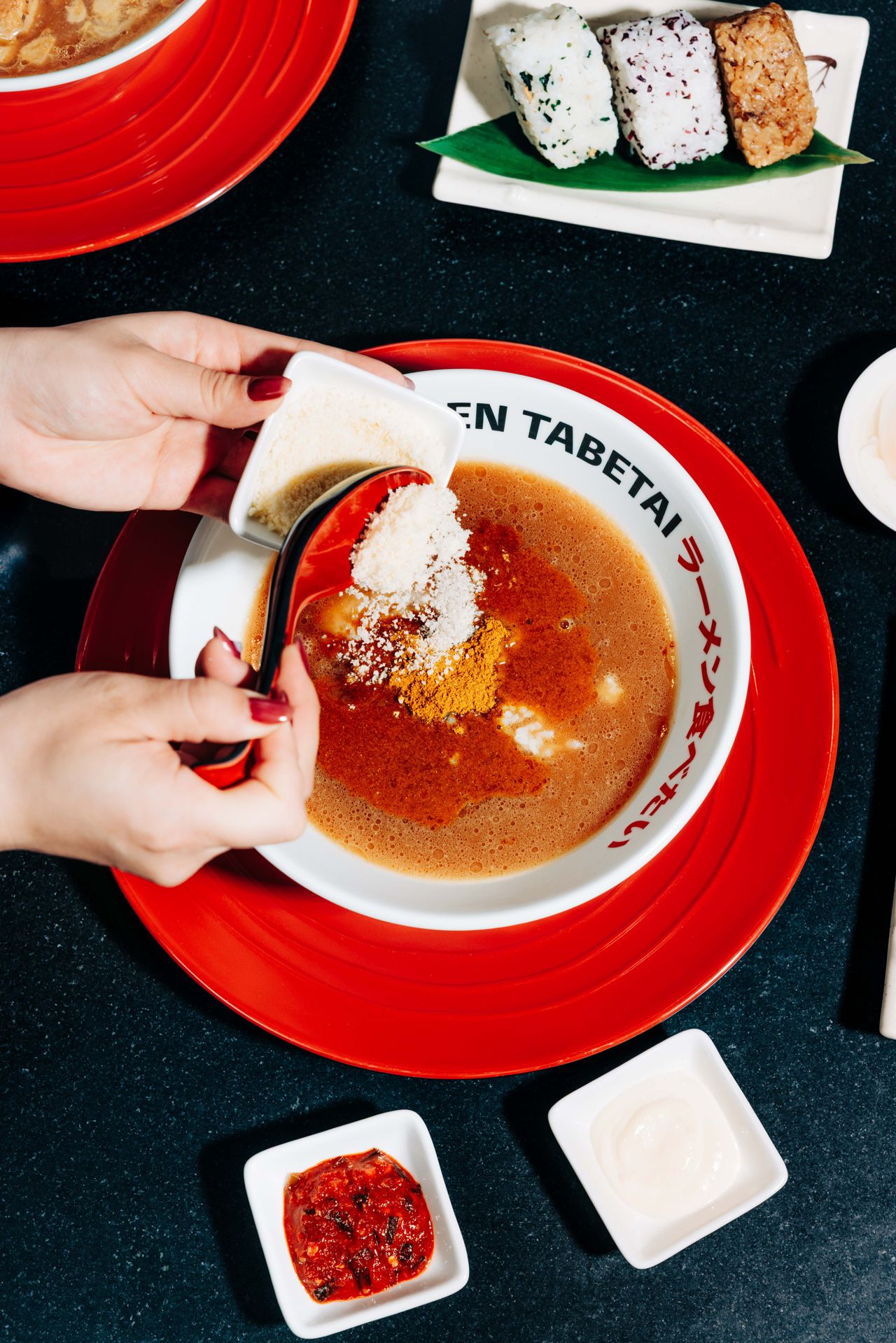 A person adds grated parmesan cheese into a bowl of broth with rice and Japanese curry powder