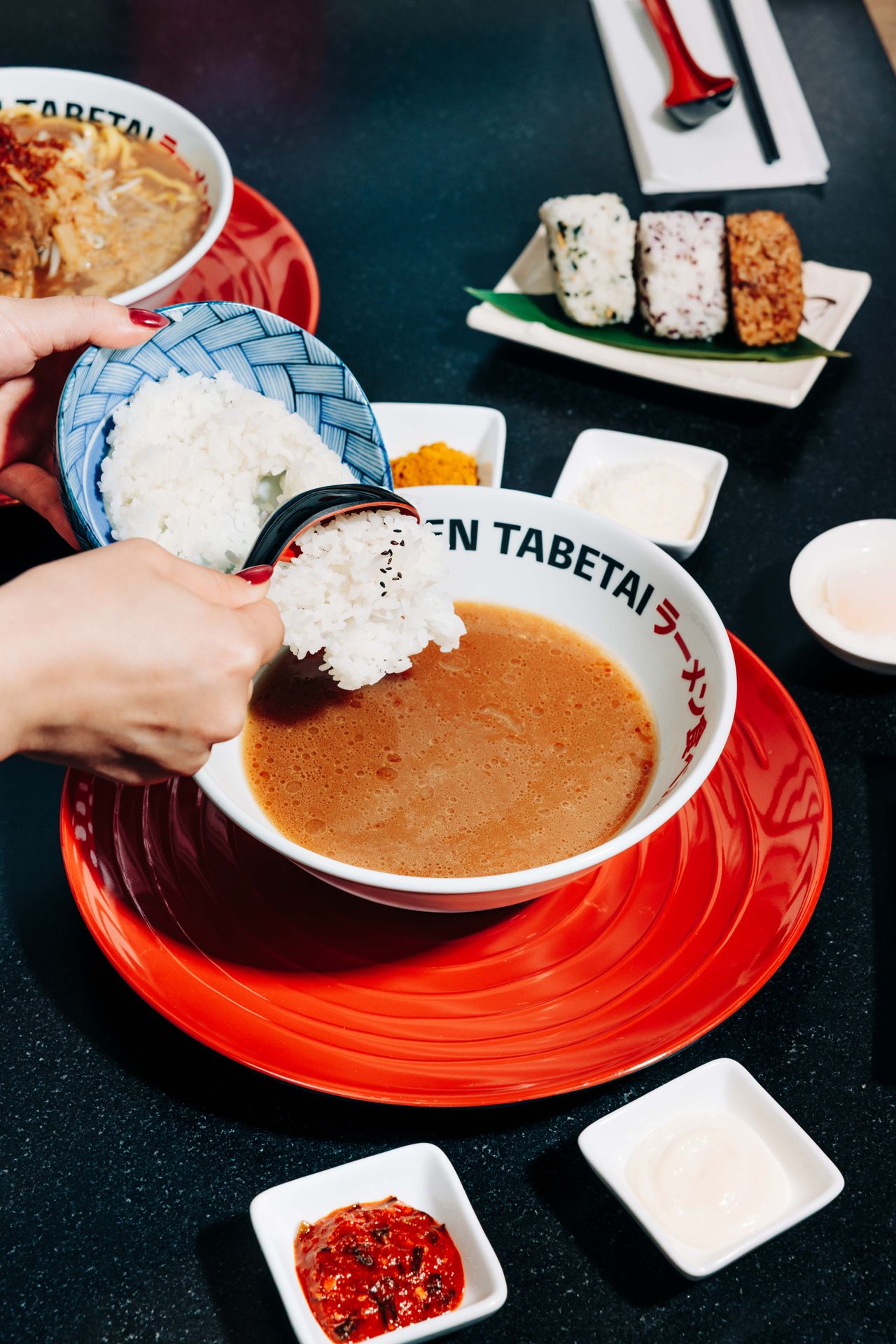 A person scoops rice into a bowl of broth