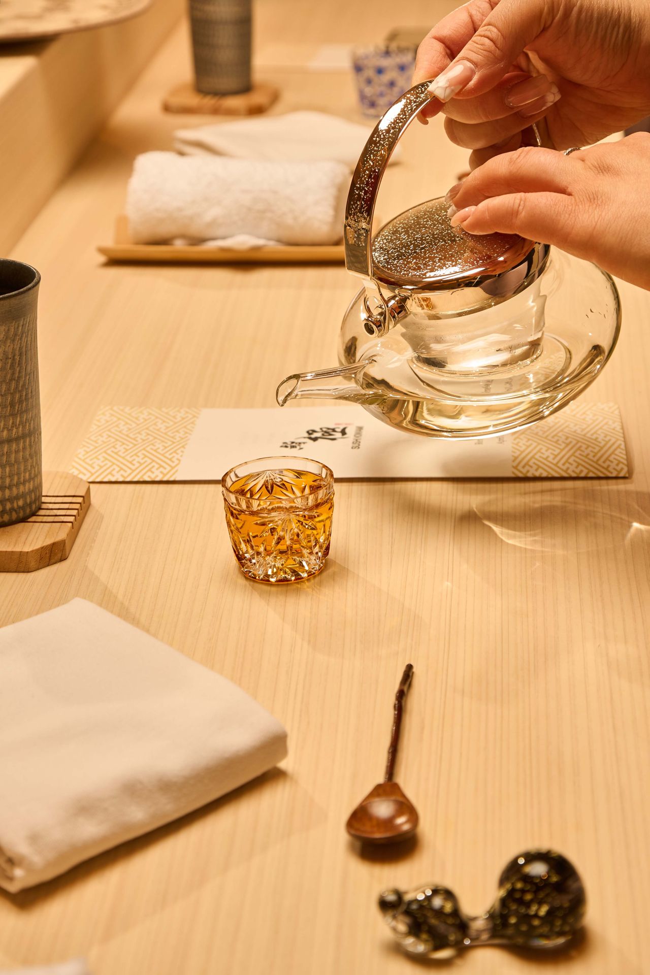 Sake is poured from a glass pot into a crystal cup
