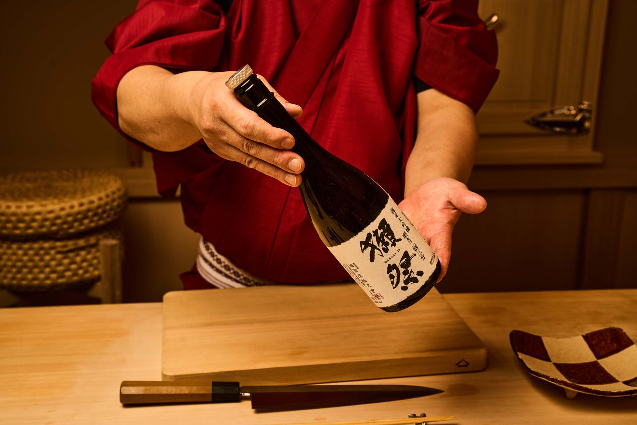 A sushi chef holds a bottle of Dassai sake