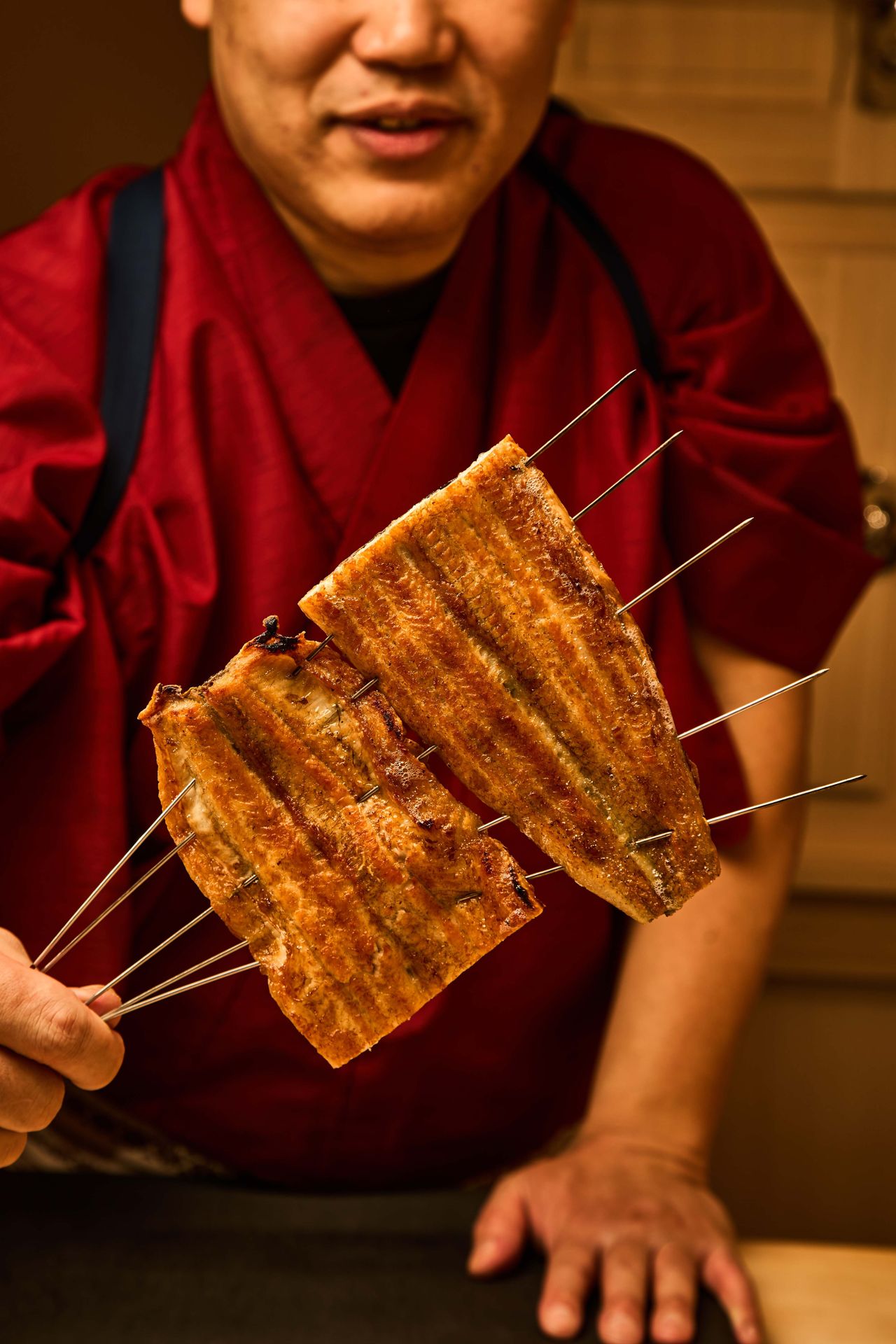 Arase holds up skewers of grilled freshwater eel