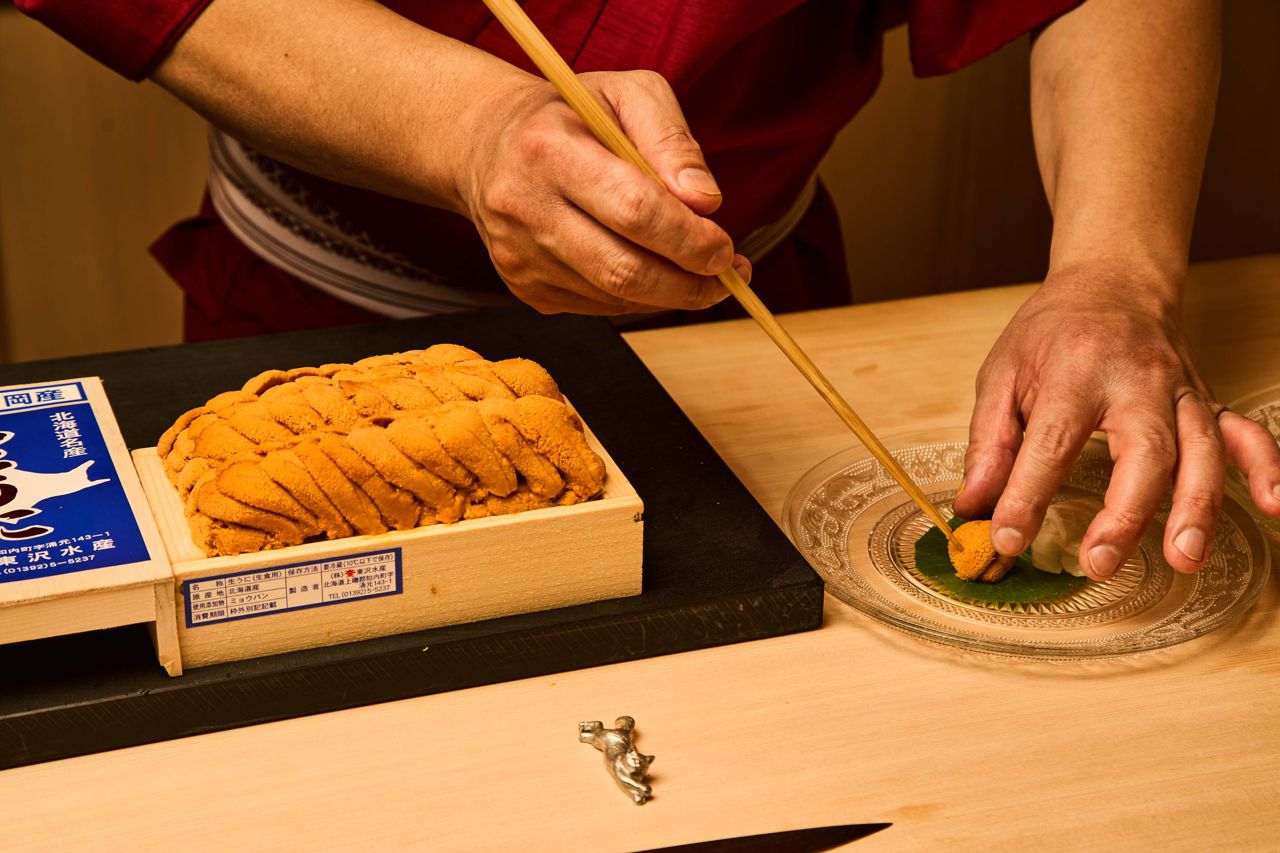 A chef uses chopsticks to place a lobe of sea urchin on a plate