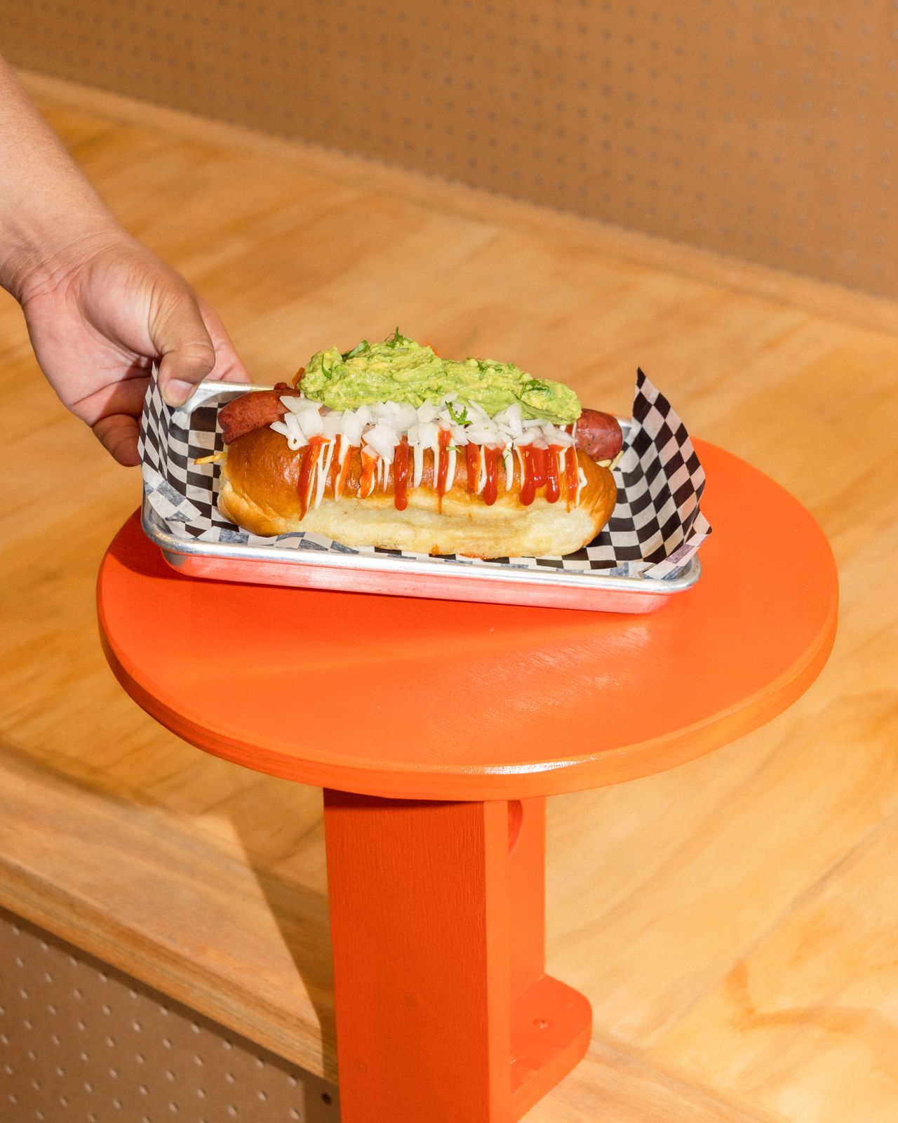 A person places a hot dog on a table at Tino's