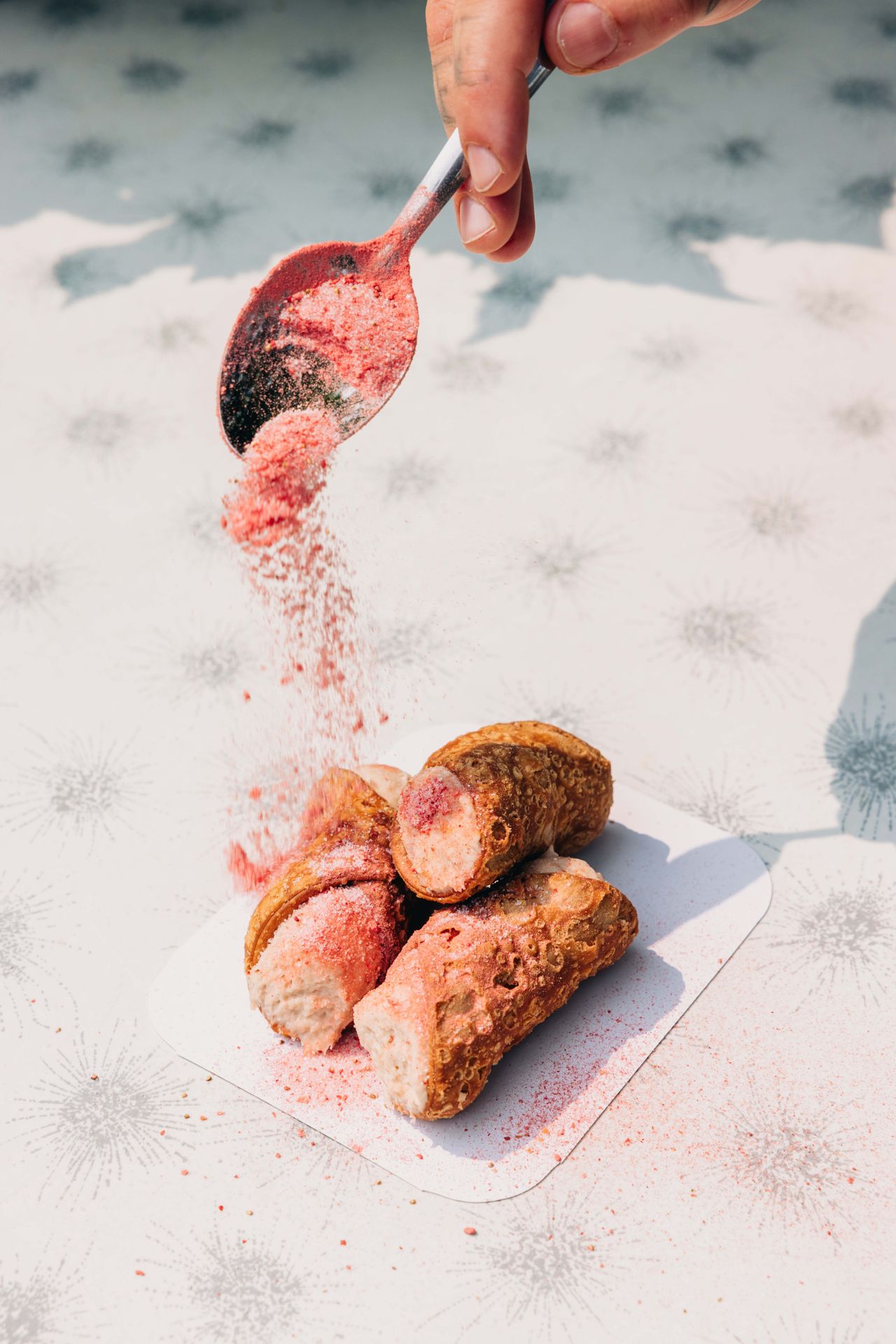 A person dusts cannoli with coloured sugar