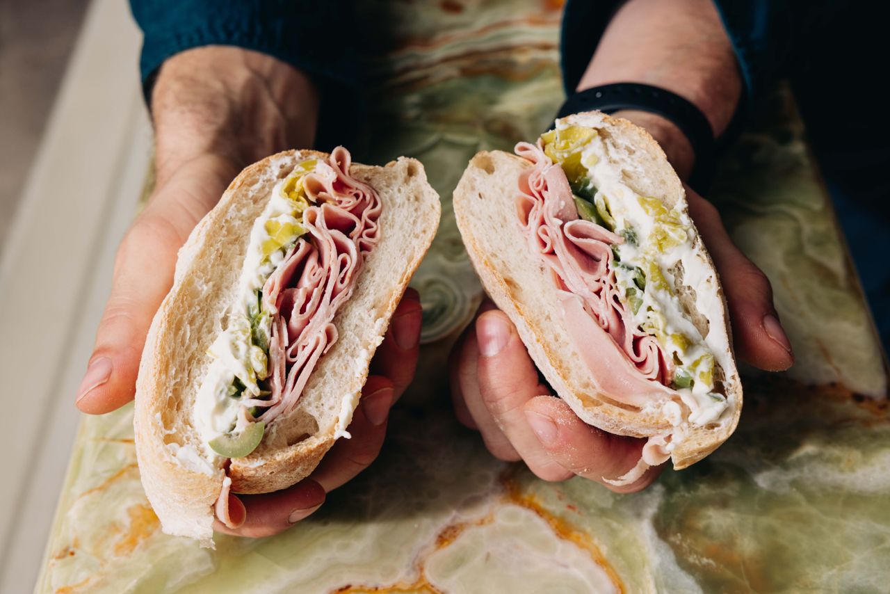 A person holds two halves of a mortadella sandwich