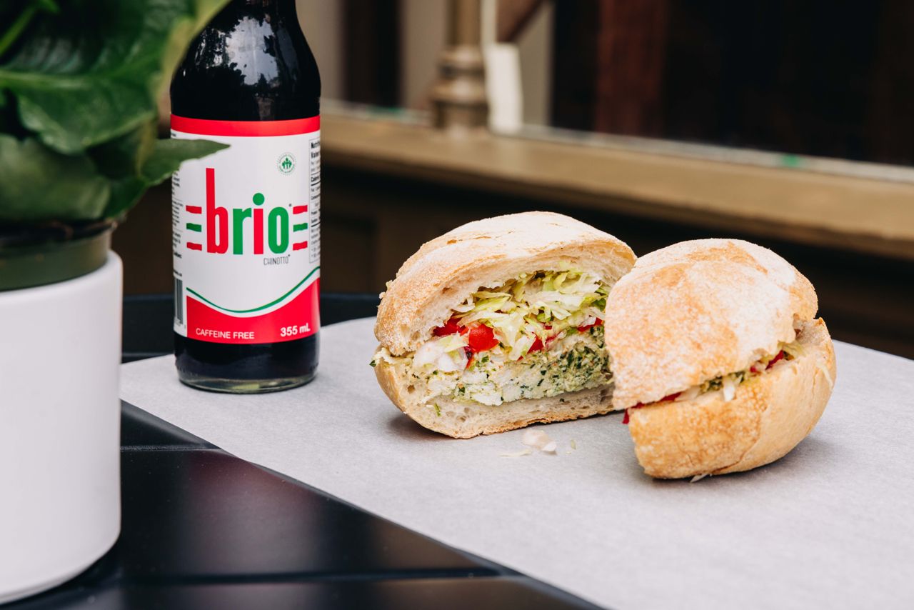A veggie sandwich next to a bottle of Brio