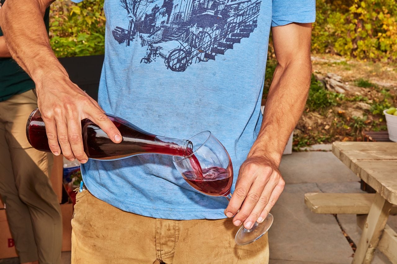 A person pours wine from a bottle into a glass at Domaine Lespiegle in Quebec