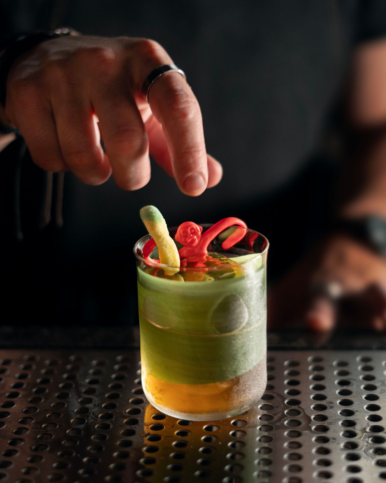 A bartender garnishes a cocktail with a gummy worm and a plastic monkey