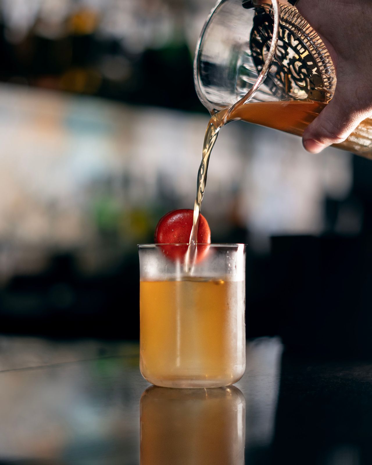 A person pours a cocktail from a mixing glass into a glass