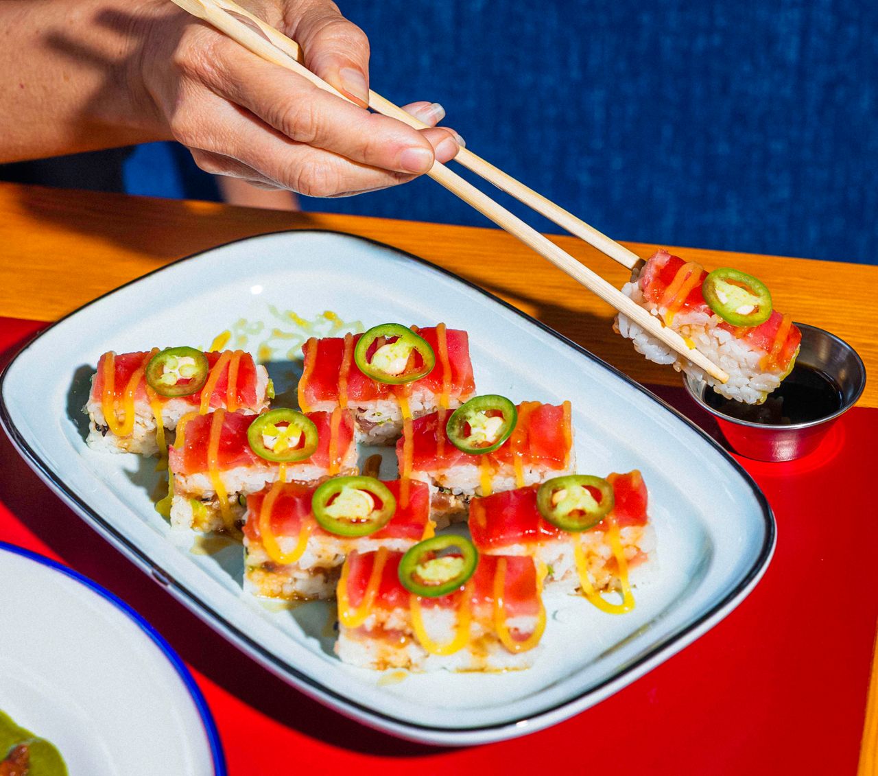 A person uses chopsticks to dib aburi sushi in soy sauce