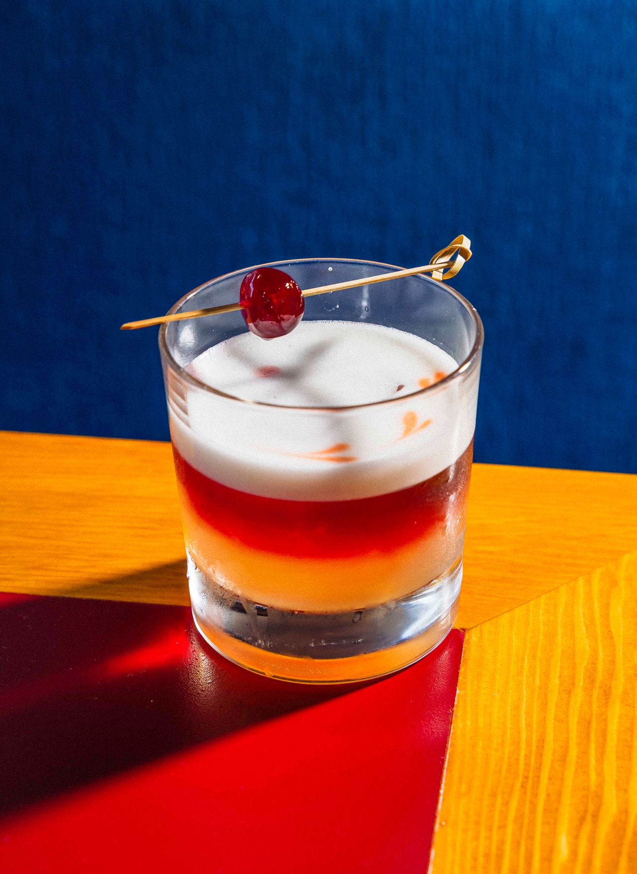 A layered sour cocktail garnished with a cherry