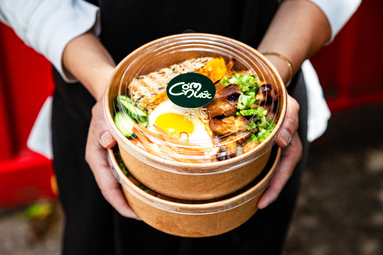 A person holds takeout containers full of Vietnamese food