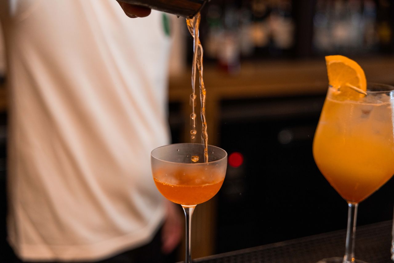 A bartender pours a cocktail from a shaker into a coupe