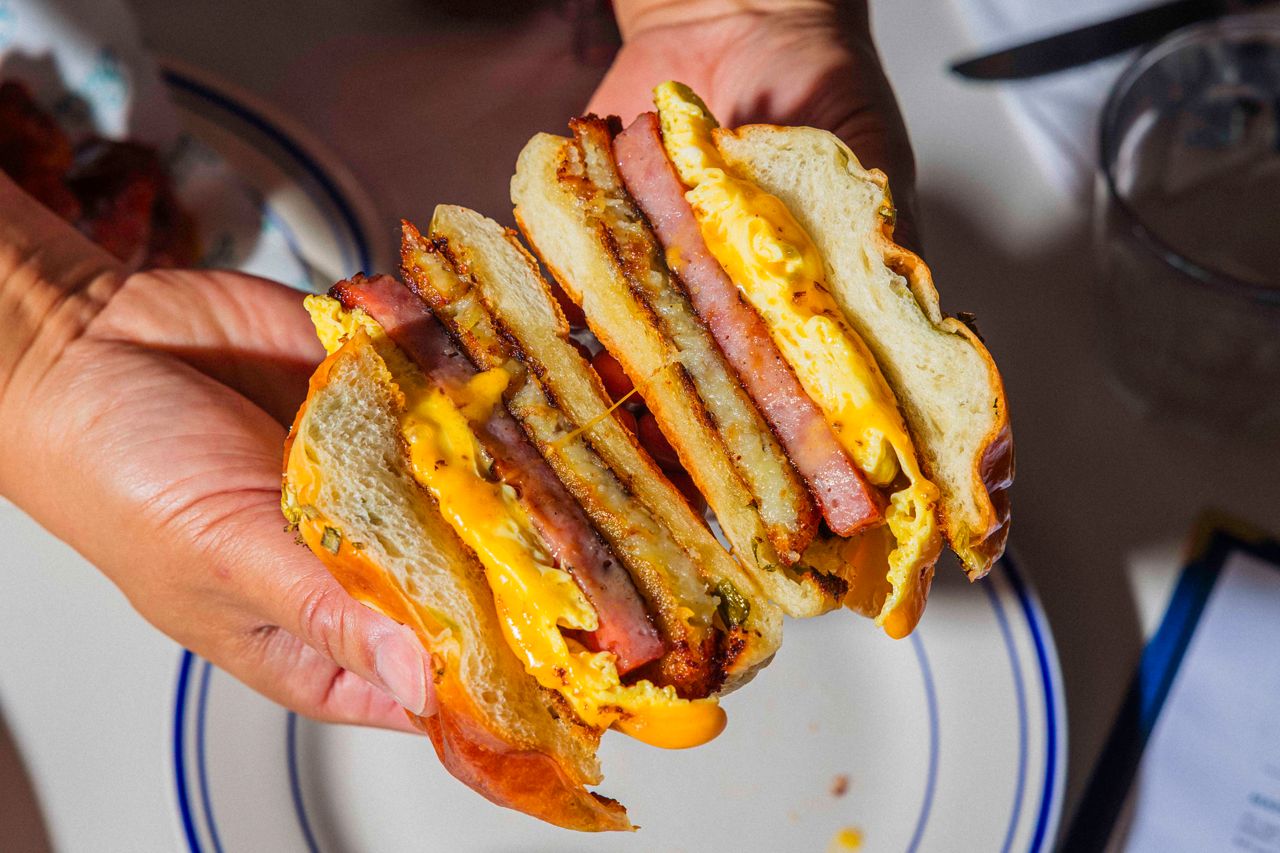 A person holds two halves. of a breakfast sandwich