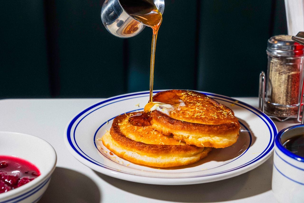 A person pours syrup over lemon-ricotta pancakes