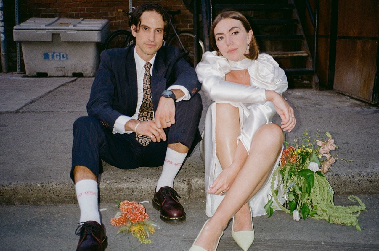 Brjánn and Ryanne sit on a street curb in their wedding outfits.