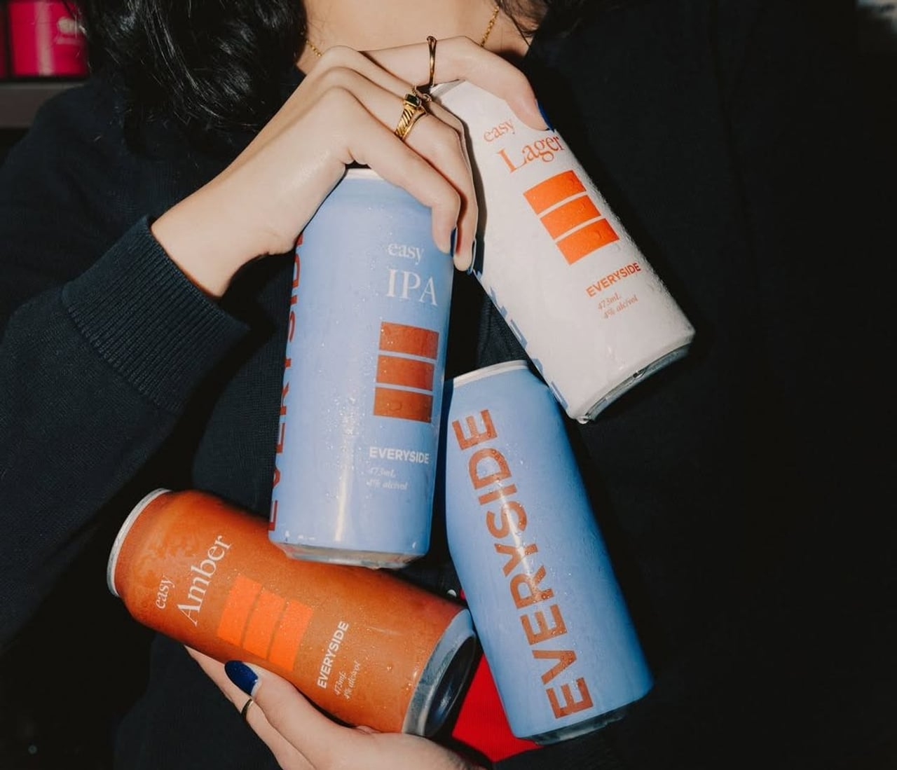 A person holds four cans of Everyside beer
