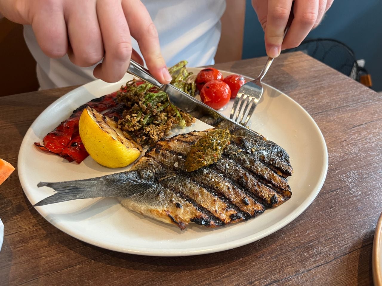 A person uses a knife and fork to cut into a whole grilled branzino