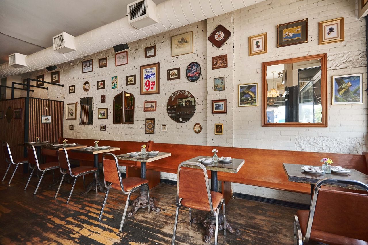 Two-top tables line one wall of the dining room at Daisy May's and the walls are decorated with mirrors and framed art
