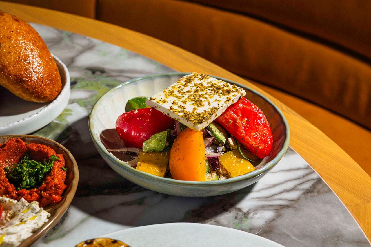 The Greek Village Salad features a sweet and firm selection of heirloom tomatoes, kalamata olives and chunks of crunchy cucumber, red onion and green peppers, topped with a slab of Greek feta