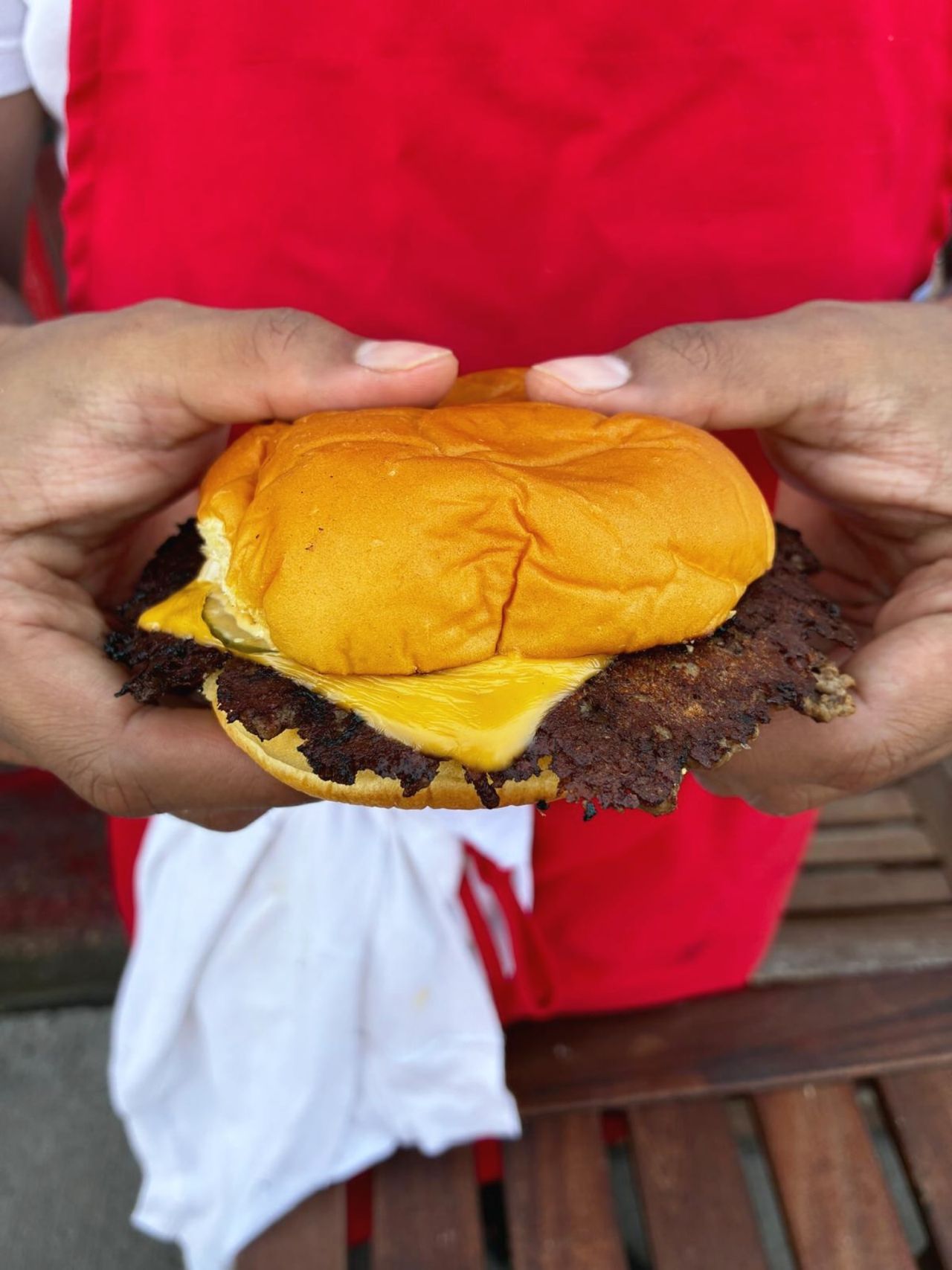 A person holds a smash burger topped with cheese