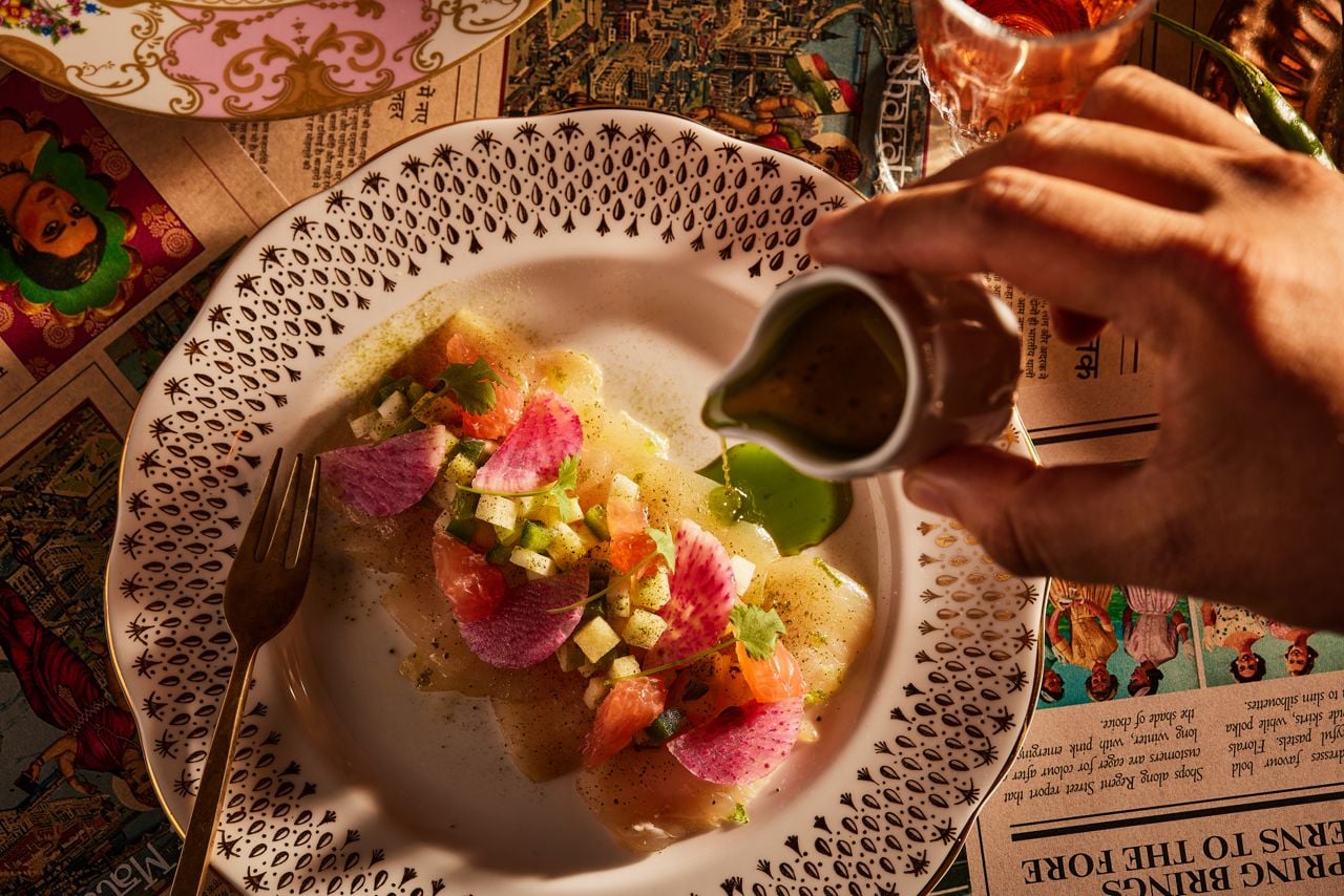 A person pours dressing over a dish at Punch, an Indo-British restaurant inside Le Germain Toronto