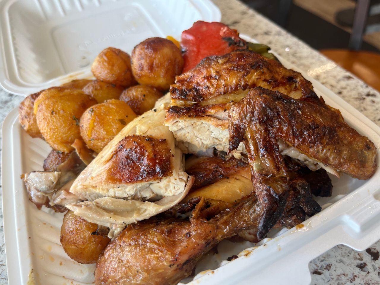 A combo meal of Portuguese chicken, potatoes and roasted vegetables in a takeout container