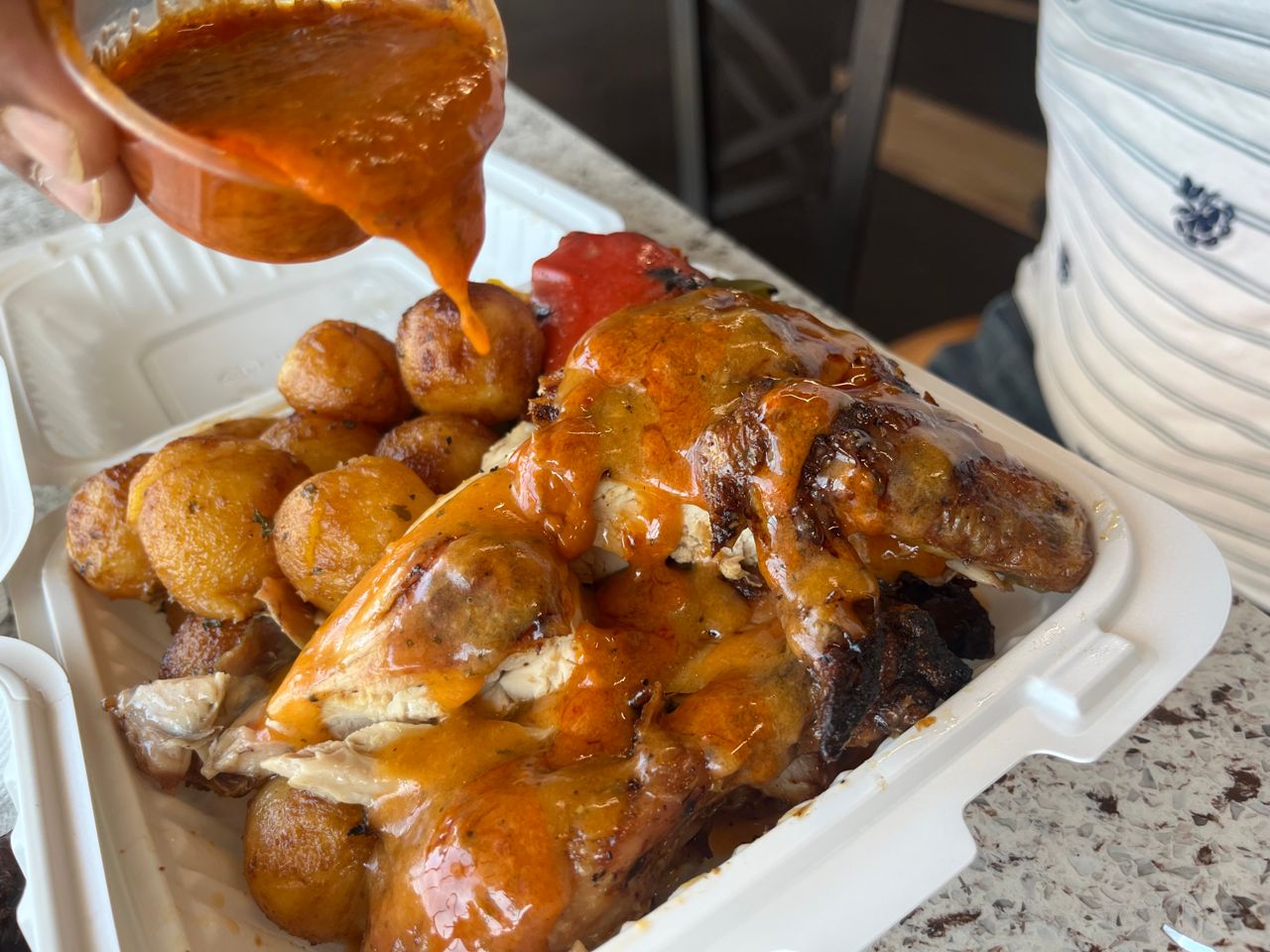 A person pours piri-piri sauce over Portuguese chicken