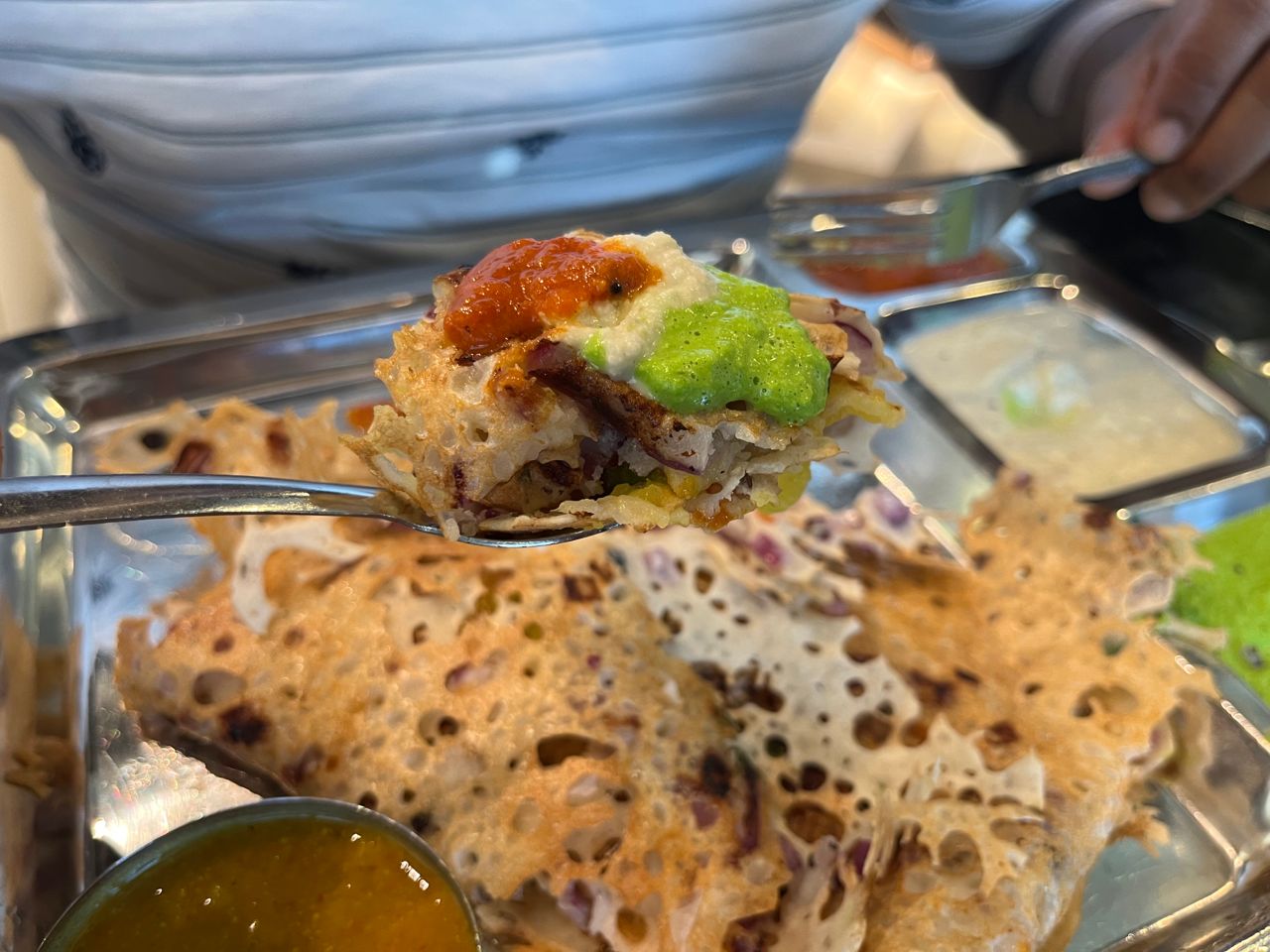 A piece of dosa covered in sauces on a fork