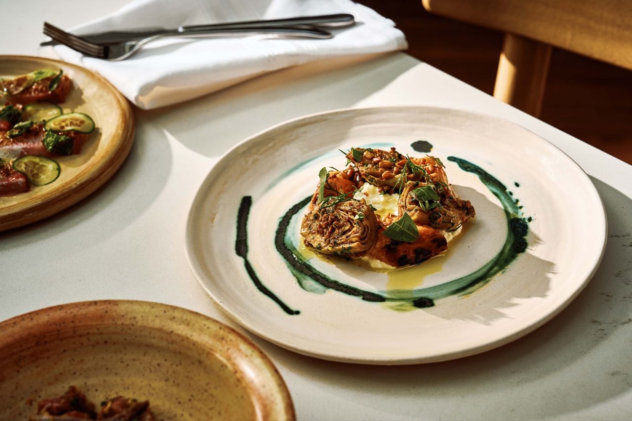 Chunks of pickled artichokes sit alongside juicy peaches on a stracciatella bed
