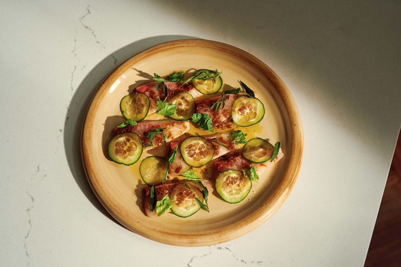 Kombu-and lime-cured hiramasa in a Filipino XO sauce, topped with Peruvian mint, mandolin-cut cucumber and mustard greens for freshness, and finished with a light drizzle of olive oil