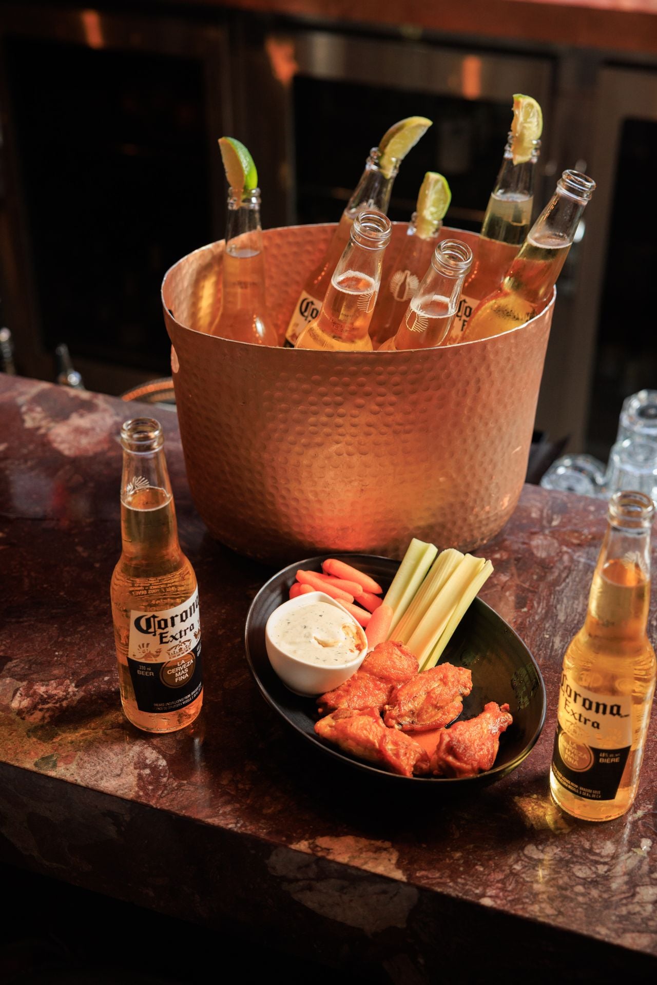 A bucket of bottles of Corona and a plate of chicken wings