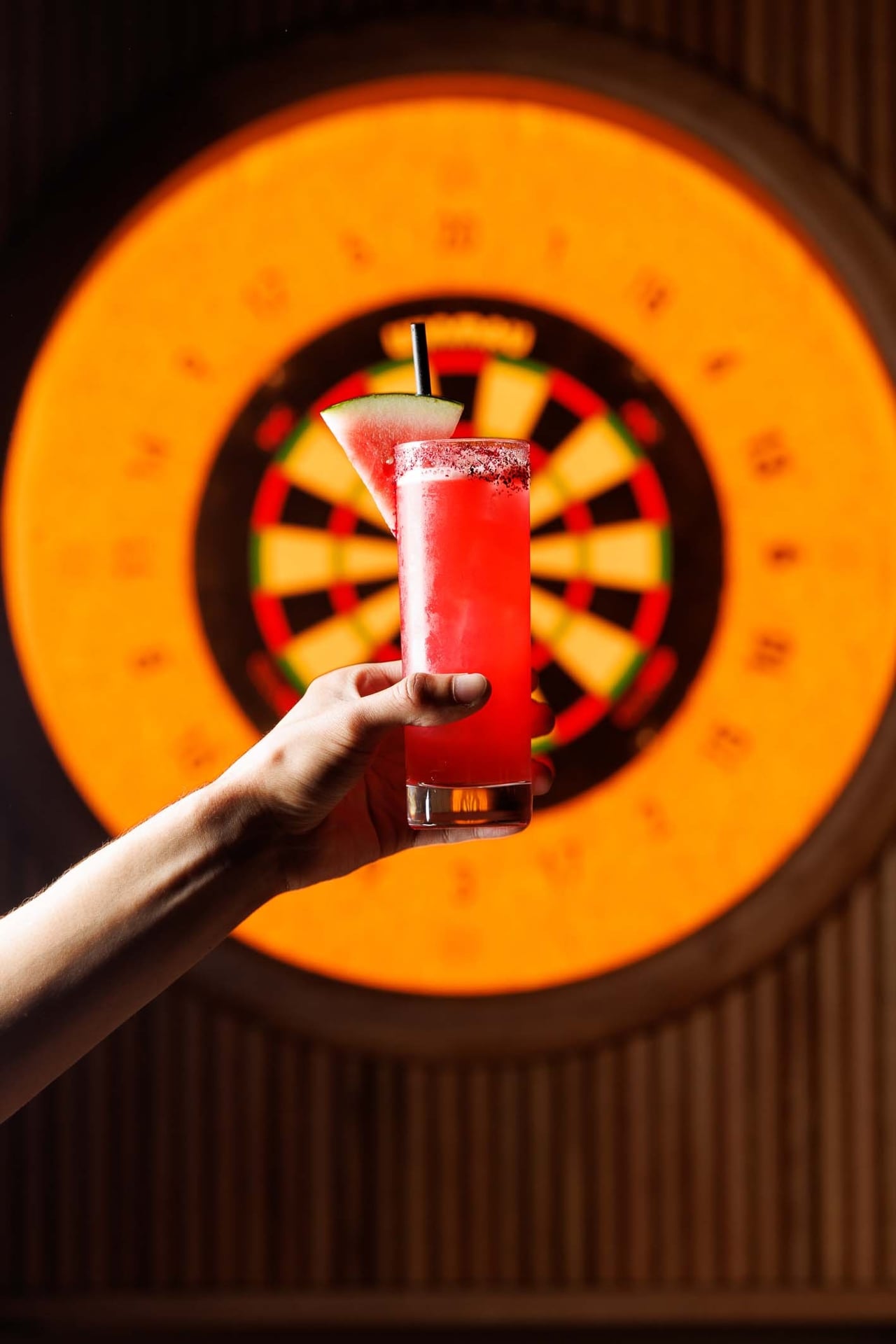 A person holds a cocktail in front of a dart board at Oche in Toronto