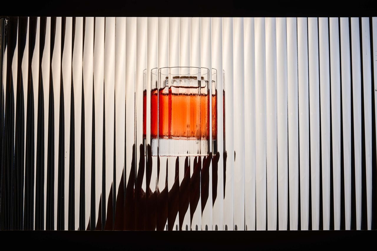 A person holds a negroni behind bevelled glass