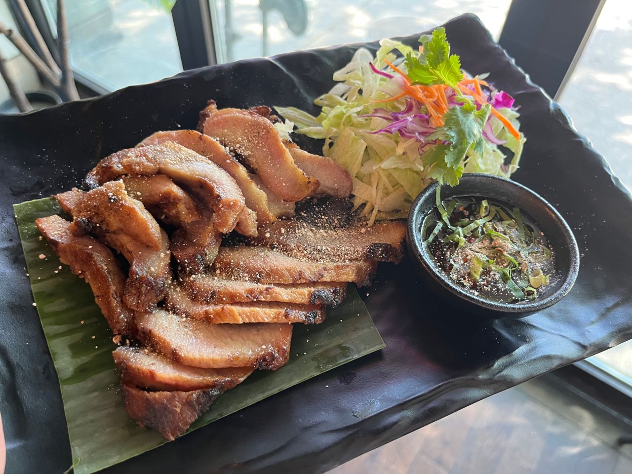A plate of roasted pork belly with a side salad and some dipping sauce