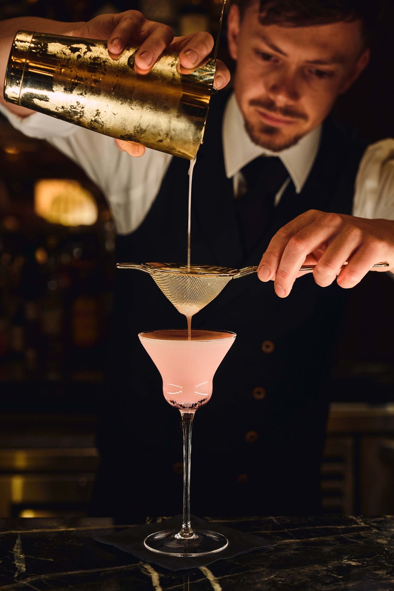 A bartender strains a cocktail into a coupe