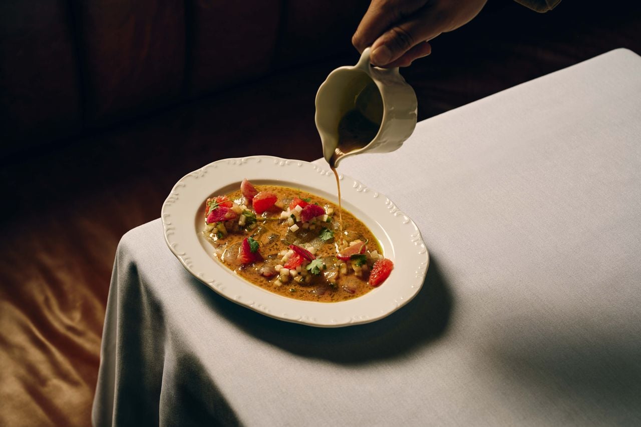 A person pours a tureen of sauce over slices of madai crudo