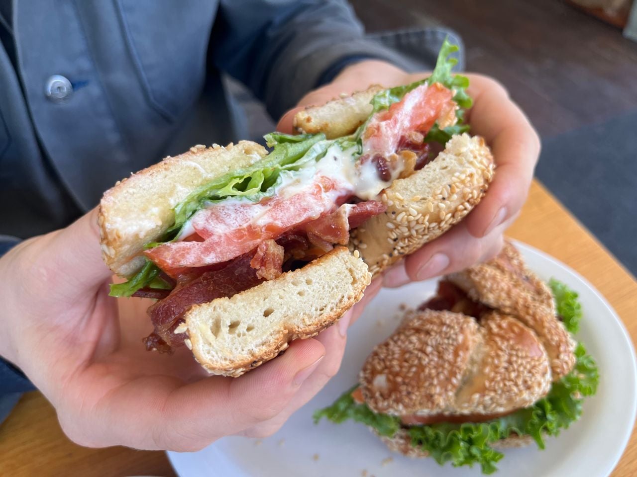 A person holds half of a bagel BLT