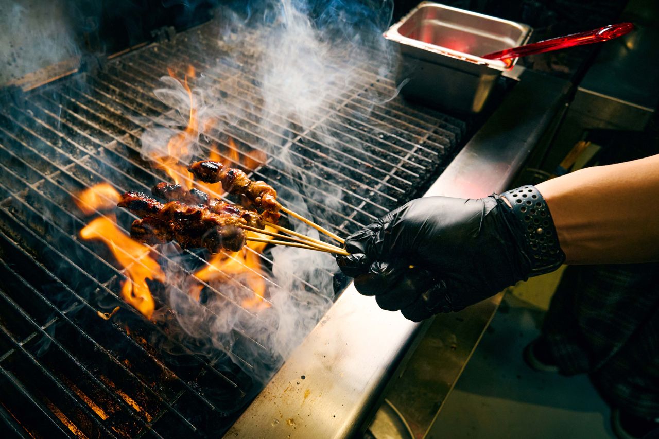 A chef wearing black gloves grills chicken skewers