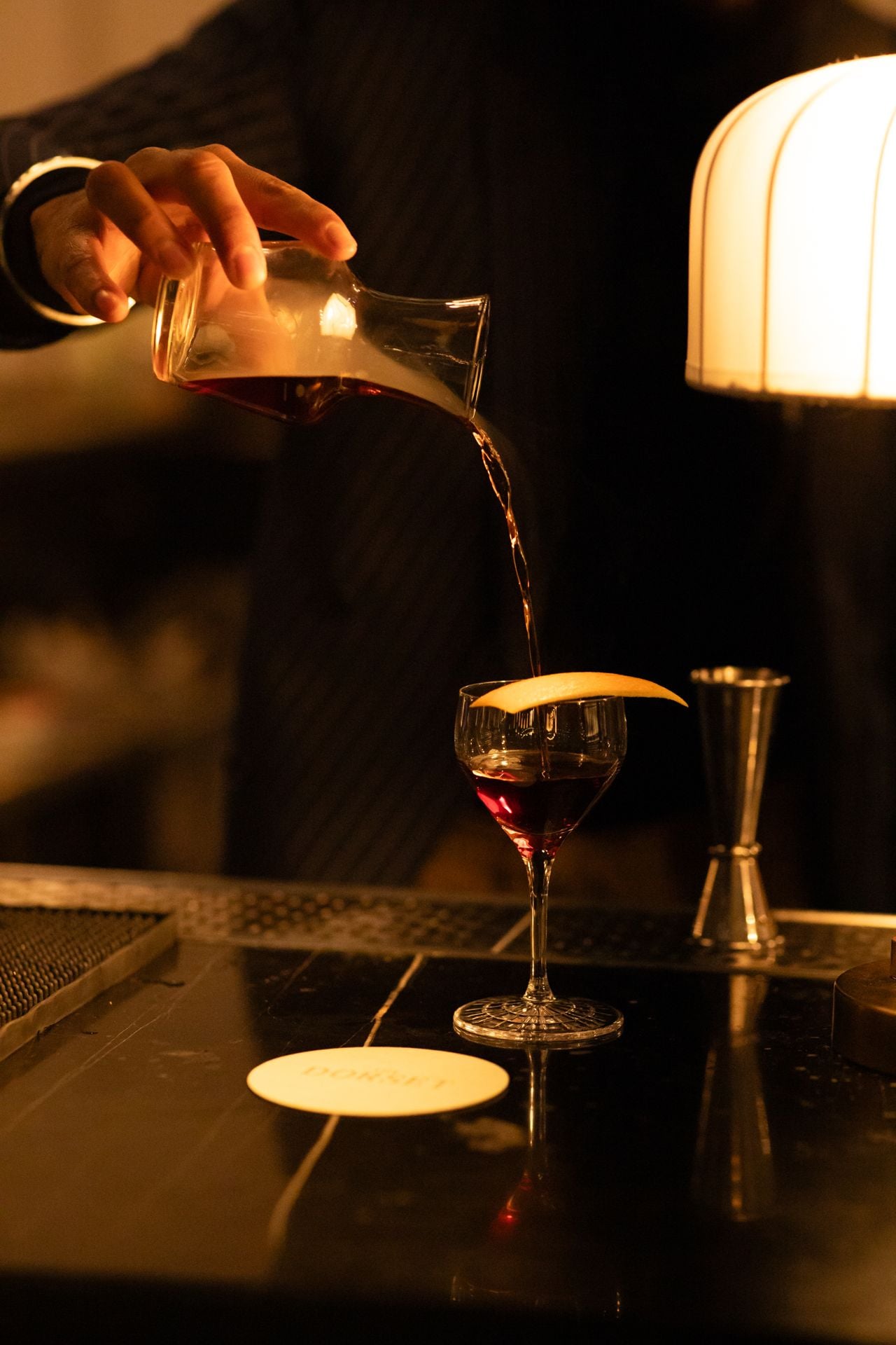 A person pours a cocktail from a carafe into a glass
