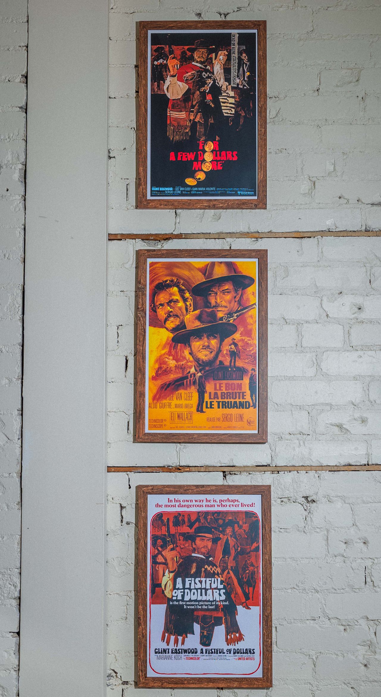 Framed movie posters hang on a white brick wall